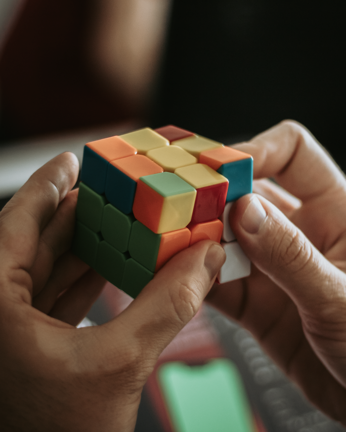 hero-img-01 Close-up of hands solving a colorful Rubik's cube indoors.